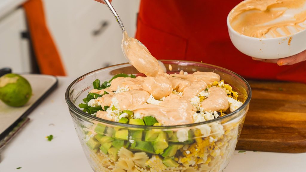 sauce being poured over top of street corn salad