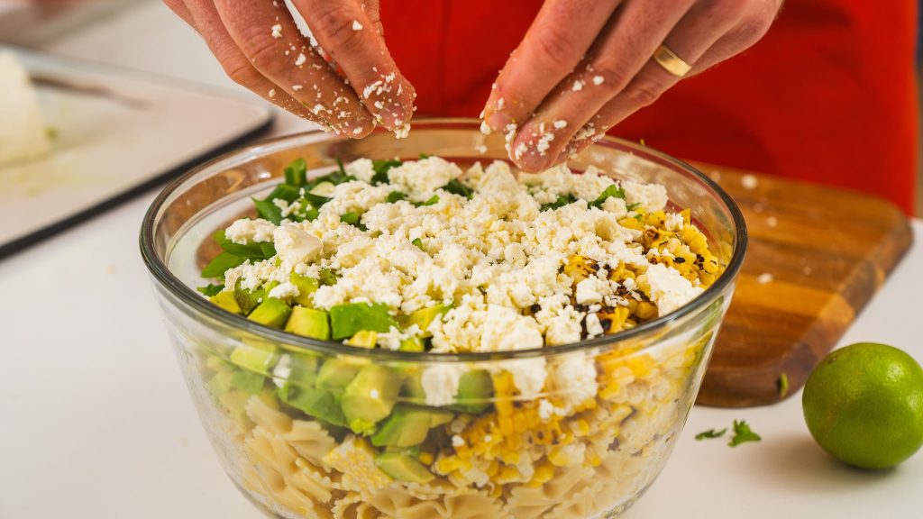 hands crumbling feta over pasta salad