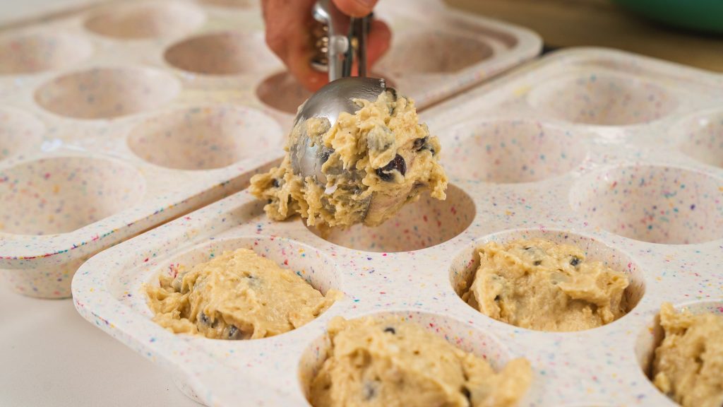 ice cream scoop schooping blueberry muffins into muffin tin