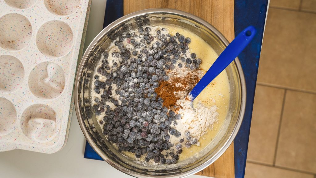 over top view of ingredients for blueberry muffins in a bowl with a blue spatula