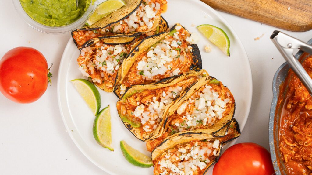 overhead shot of 5 chicken tinga tacos with lime wedges off to the side