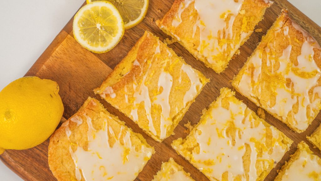 The image features a batch of lemon brownie recipe neatly cut into squares and arranged on a wooden board.