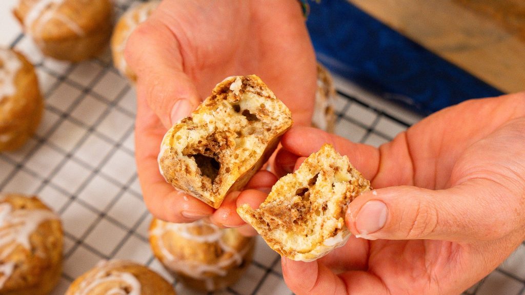 hands pulling apart cinnamon cottage cheese muffin over a wire rack