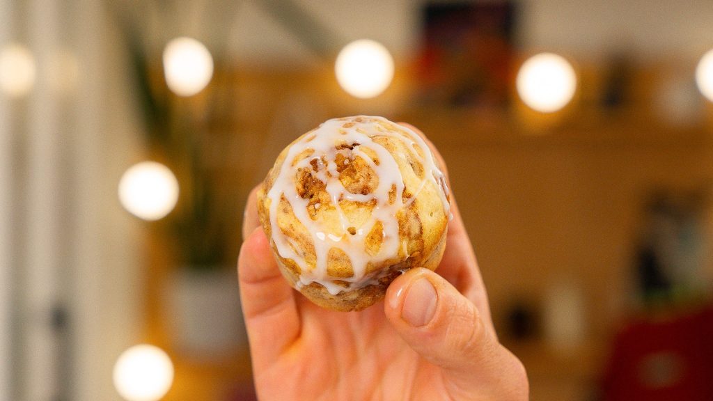 hand holding cinnamon cottage cheese muffin in front of background lights.