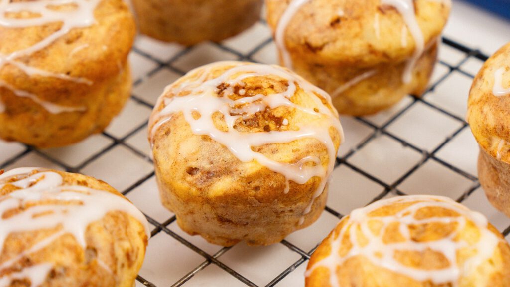 close up shot of cinnamon cottage cheese muffin with icing sitting beside 5 other muffins on a wire wrack