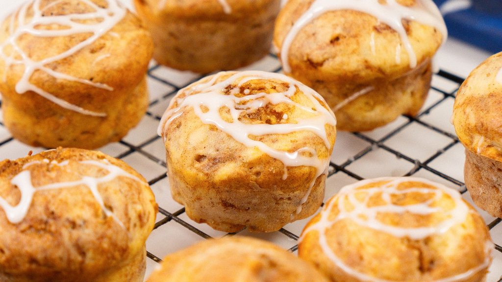 close up shot of cinnamon cottage cheese muffin with icing sitting beside 5 other muffins on a wire wrack