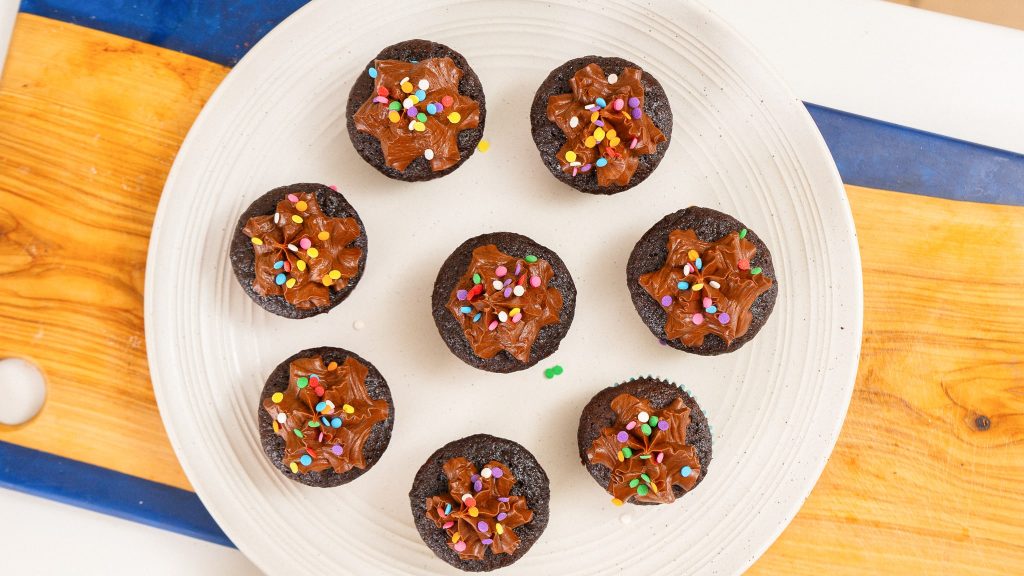 overhead shot of 8 cup cakes on a plate sitting on a wooden cutting board