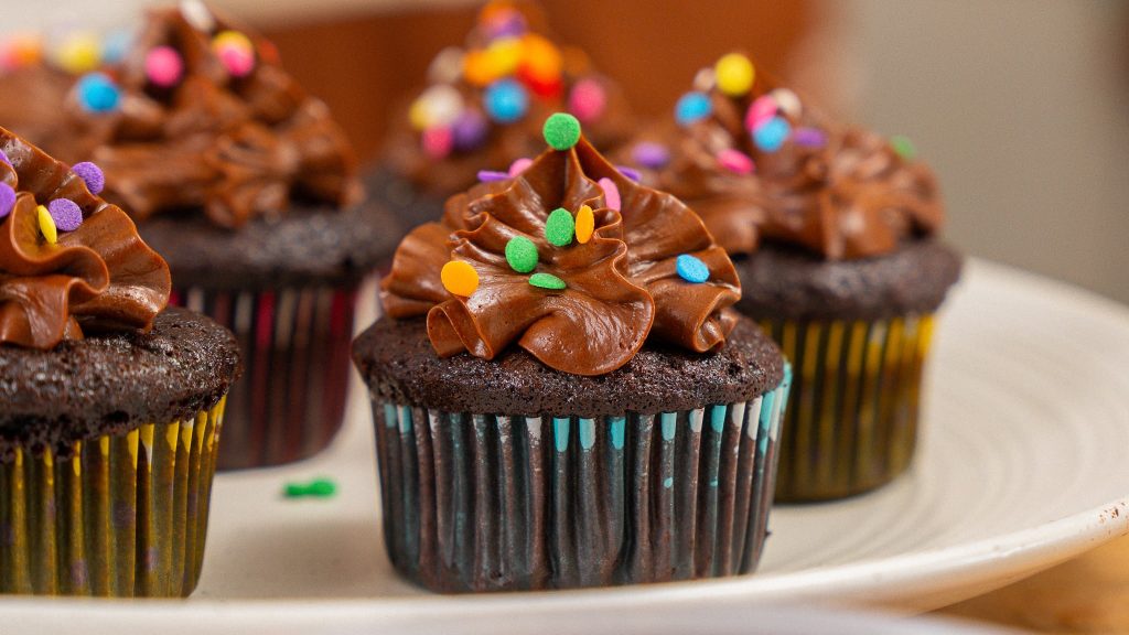 close up horizontal angle of chocolate cupcake with icing and sprinkles. Surrounded by other cupcakes