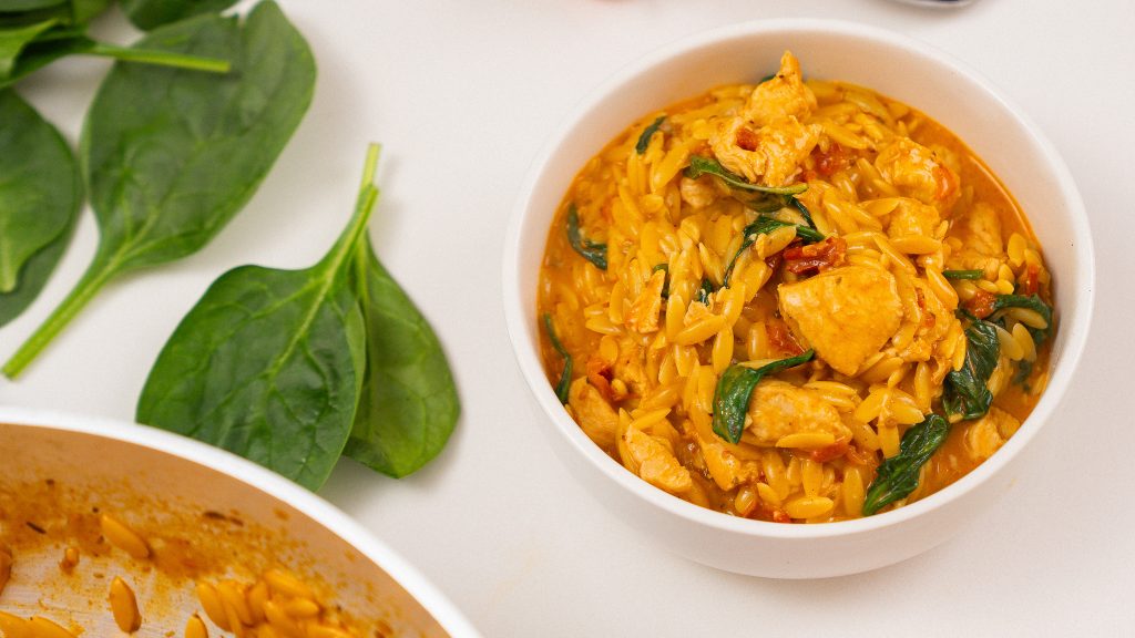 A close-up side view of a bowl of Marry Me Chicken Orzo, highlighting the creamy texture and fresh spinach mixed with chicken and orzo.