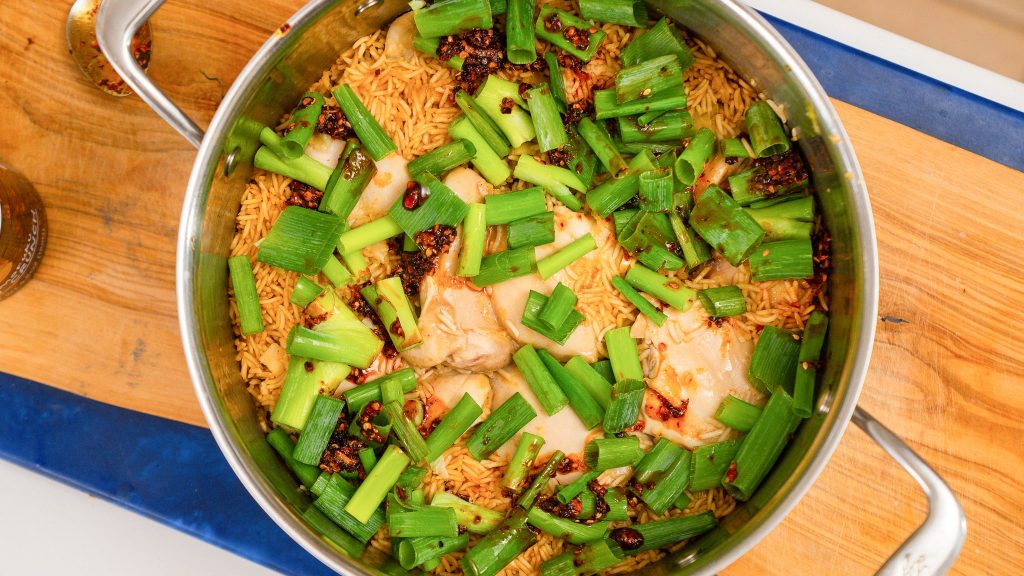 Overhead shot of pot of rice and chicken. Green onions and chilli oil are drizzled on top