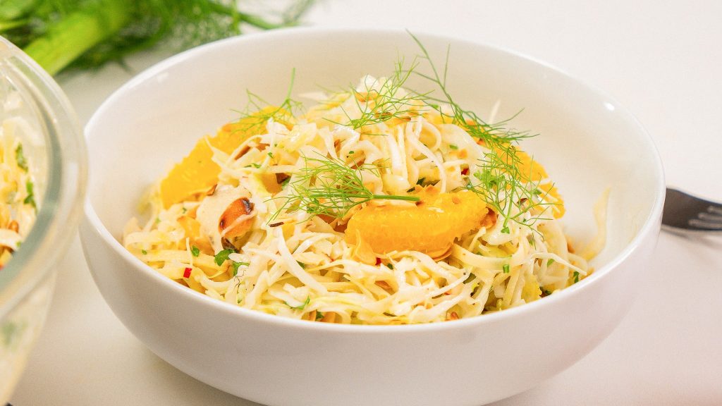 side angle shot of white bowl filled with refreshing cabbage, fennel, orange segments. Topped with fennel fronds