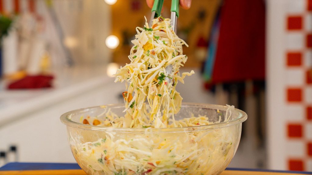 tongs picking up cabbage slaw from glass bowl