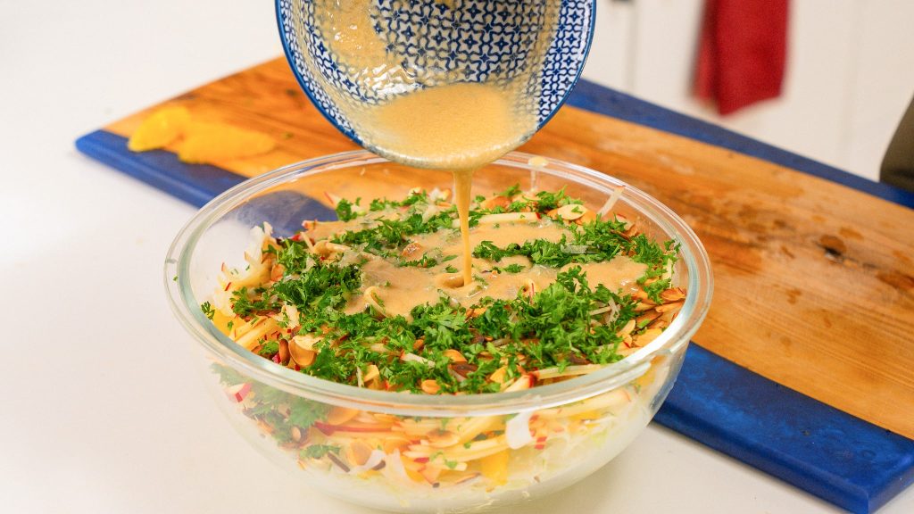 tahini dressing being poured out of a blue bowl ontop of cabbageslaw.