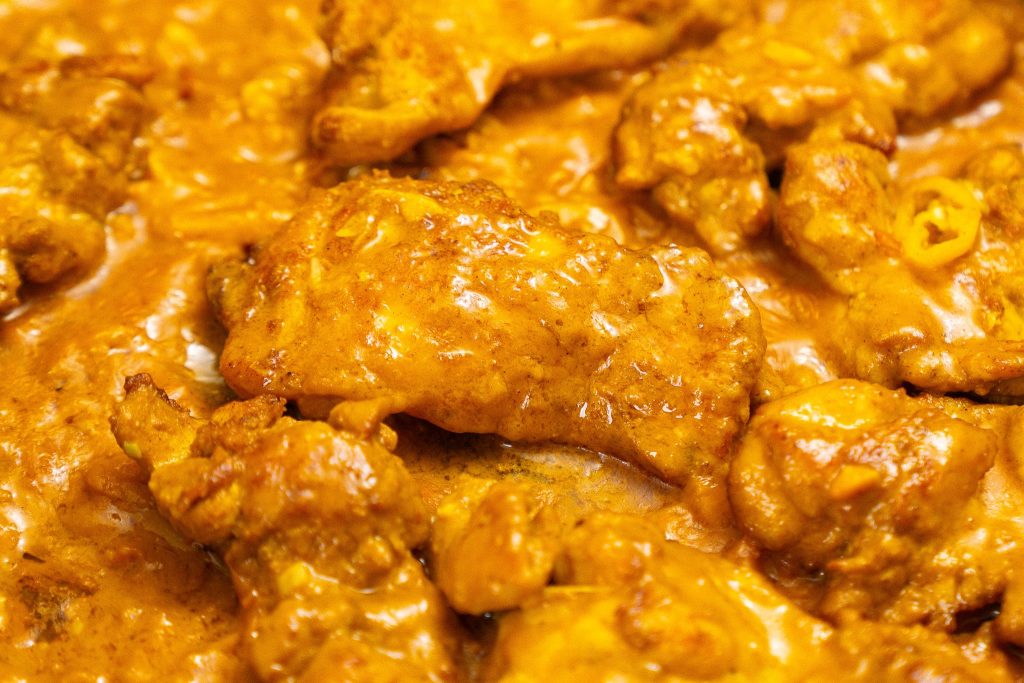 Close-up of chicken thighs coated in a rich, creamy peanut sauce, simmering in the pan