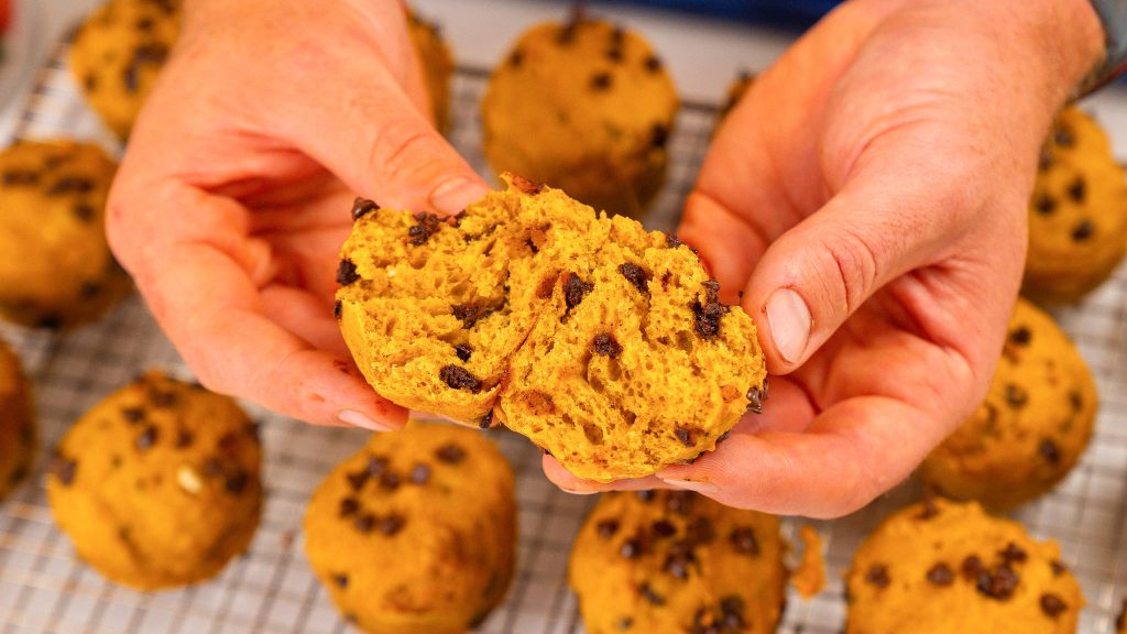 Hands breaking open a cottage cheese muffin to reveal the fluffy and moist inside, studded with mini chocolate chips, with more muffins in the background.