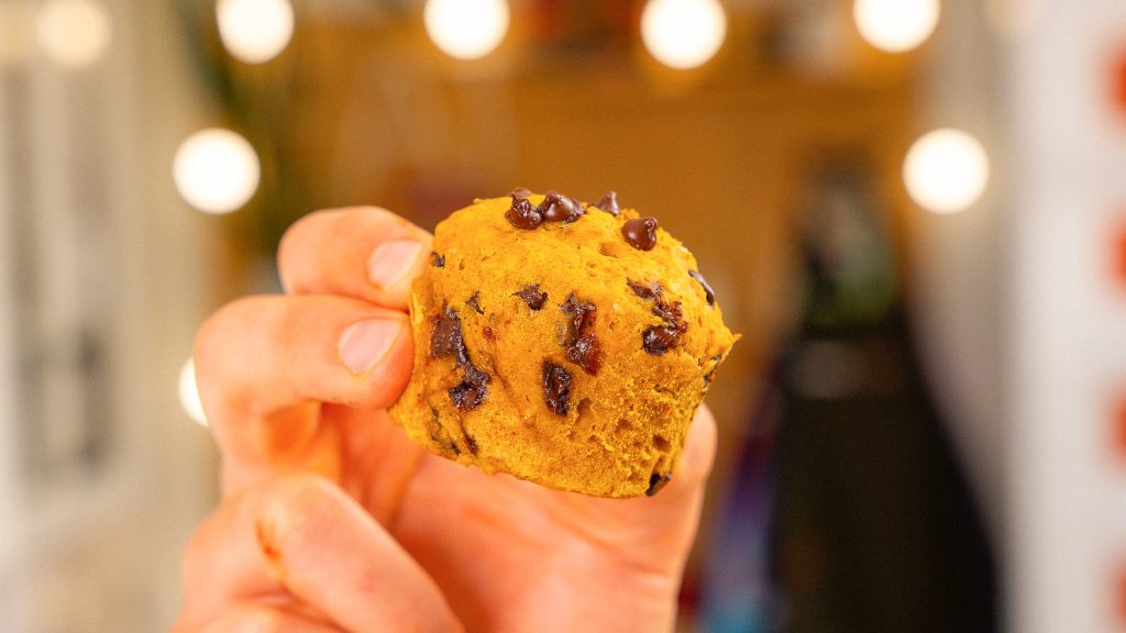 A hand holding a single recipe, showing its round, soft texture with melty chocolate chips.