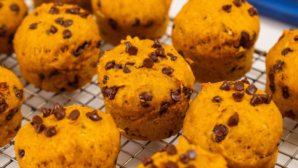 Rows of healthy pumpkin cottage cheese muffins cooling on a wire rack, with some mini chocolate chips melting on top.