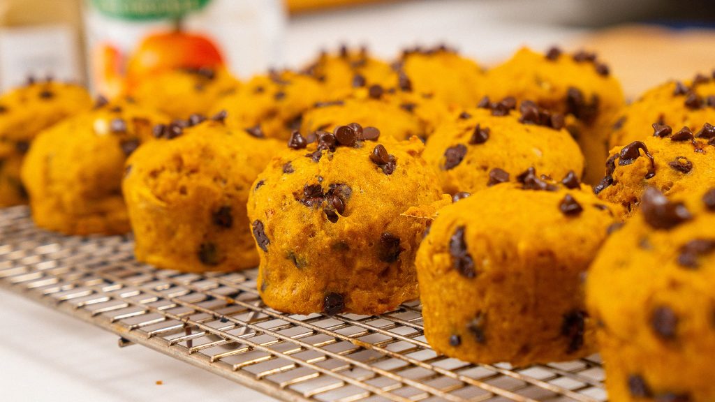 A close-up view of healthy muffins topped with mini chocolate chips, still in the speckled muffin tray, showing their soft texture.