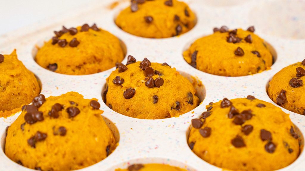 Close-up of freshly baked cottage cheese muffins with chocolate chips, sitting in the muffin tray on a baking sheet.