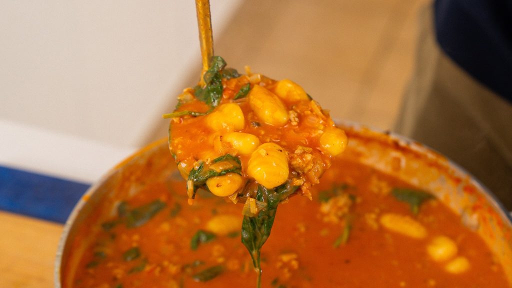 A ladle filled with gnocchi, sausage, and spinach in a rich tomato broth being lifted out of a pot of chicken sausage gnocchi soup.