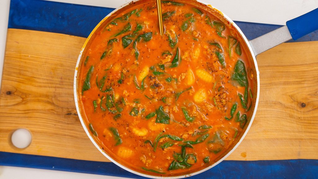 A pot of simmering chicken sausage gnocchi soup, with visible gnocchi and spinach floating in a tomato-based broth, ready to be served.