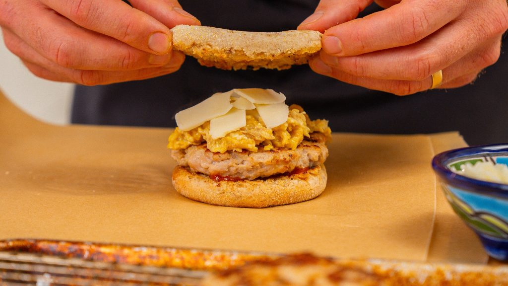 hands placing top of an english muffin onto a breakfast sandwich