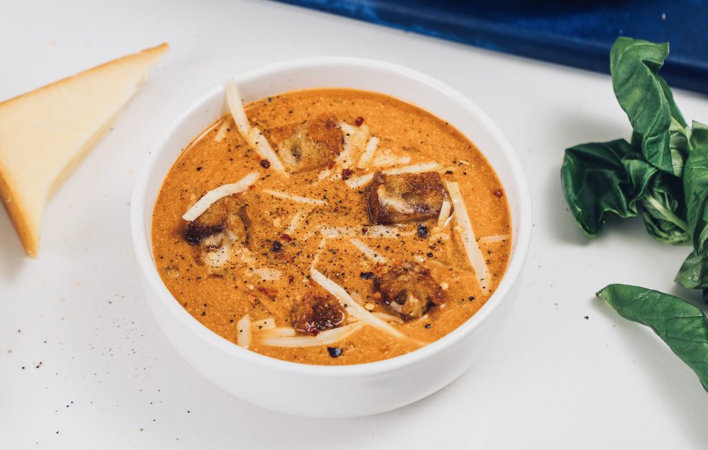 Top down view of tomato soup in white bowl with croutons and cheese on top