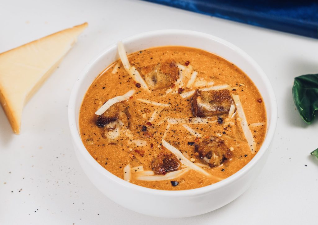 Top down view of tomato soup in white bowl with croutons and cheese on top