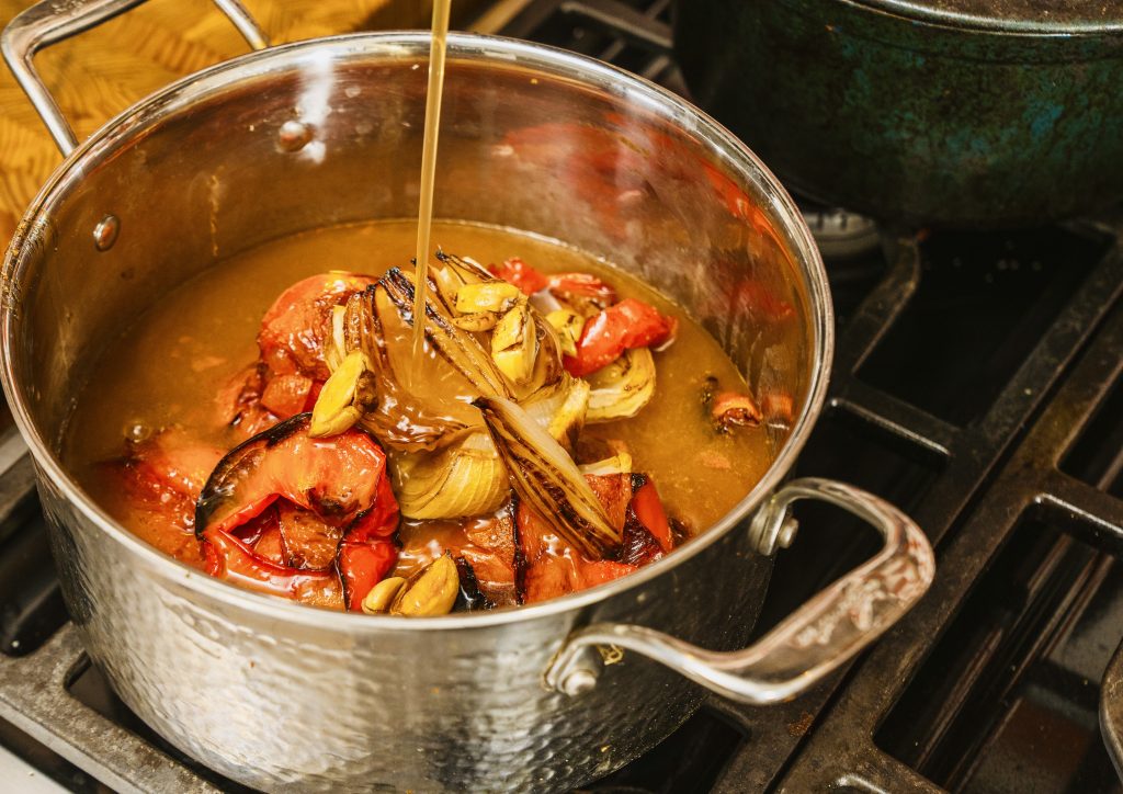 stock being poured into pot on stove with roasted ingredients inside.