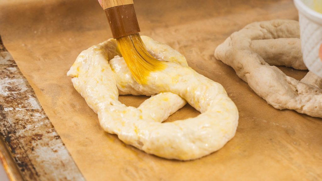 pastry brush being used to brush egg wash on to uncooked pretzel