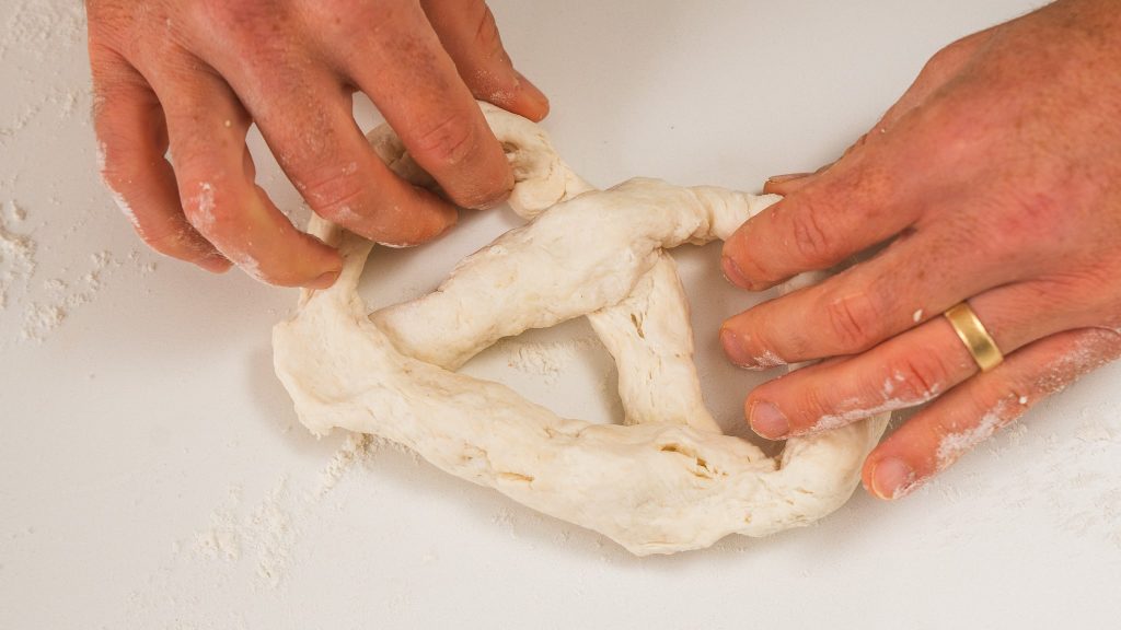 hand shaping dough into a pretzel shape