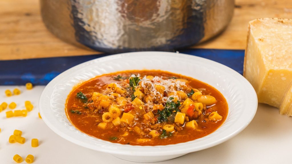 side angle image of stanly tucci soup. Parmesan block to the left, pot in background. 