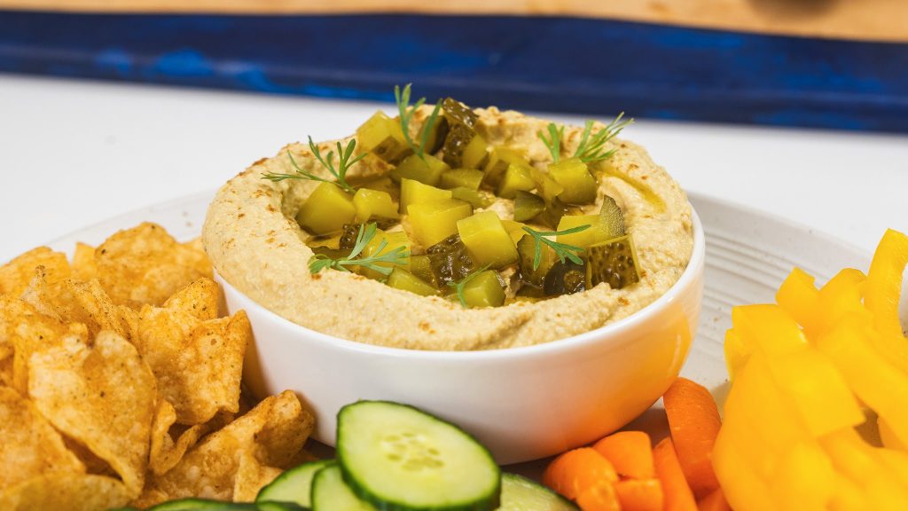 side angle view of dill pickle hummus in bowl surrounded by veggies