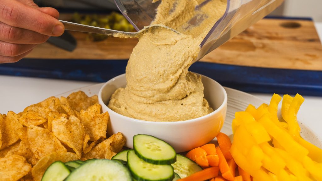 hummus being poured into white bowl from blender bowl