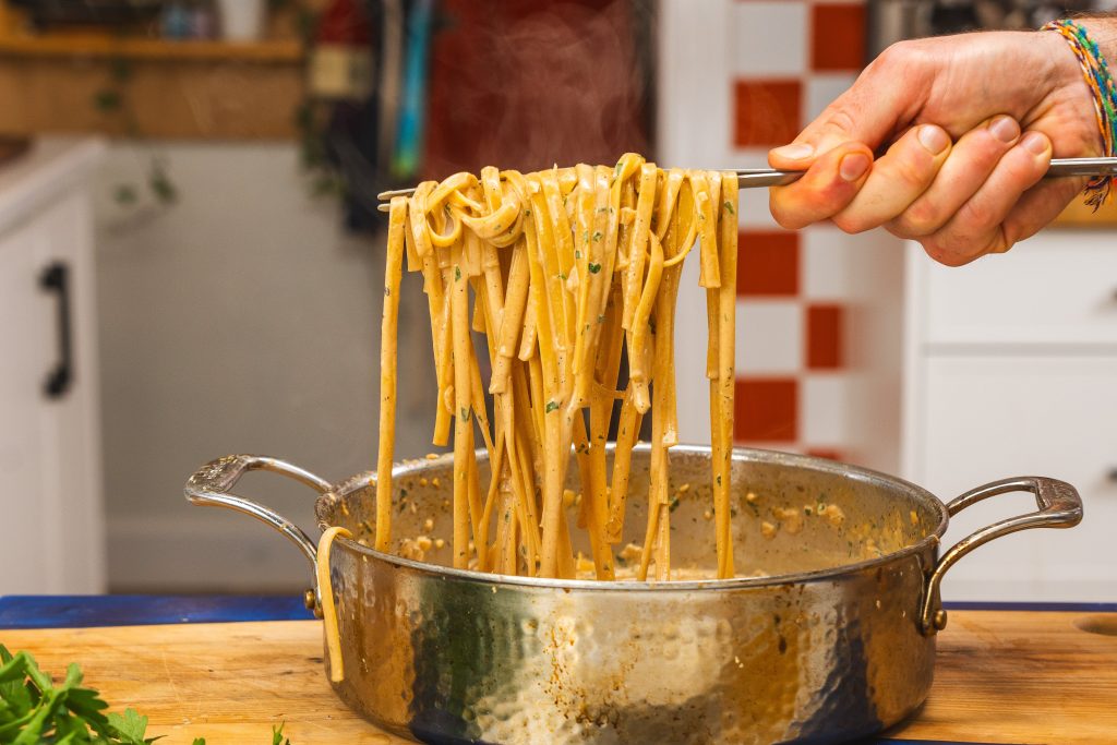 A stainless steel pot of homemade fettuccine alfredo being scooped up with a serving spoon.