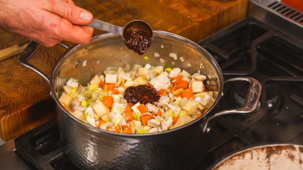 A pot filled with diced carrot, celery and onions with a scoop of chipotle chilis in adobo being added.