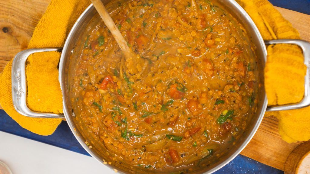 A saucepan with a wooden spoon on the side full of homemade red lentil dalh.