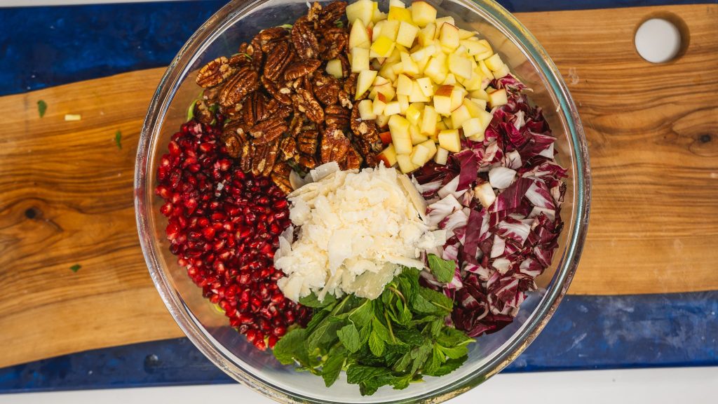 Overhead bowl of salad ingredients like shaved brussels sprouts, diced apple, pomegranate seeds, radicchio and shaved parmesan.