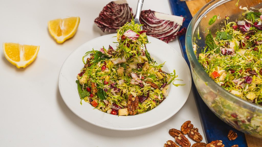 Large, white-rimmed bowl on counter with a colourful salad inside. Radicchio and pecans can be seen on the counter.