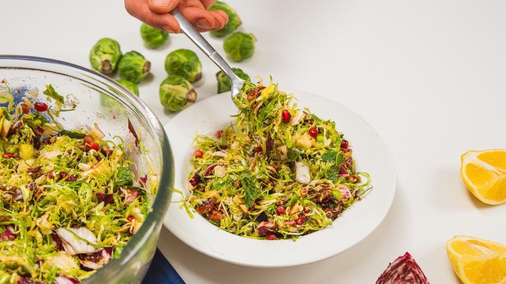 large serving bowl of colourful salad with a white bowl nearby. There is a fork in the white bowl scooping up some of the salad.