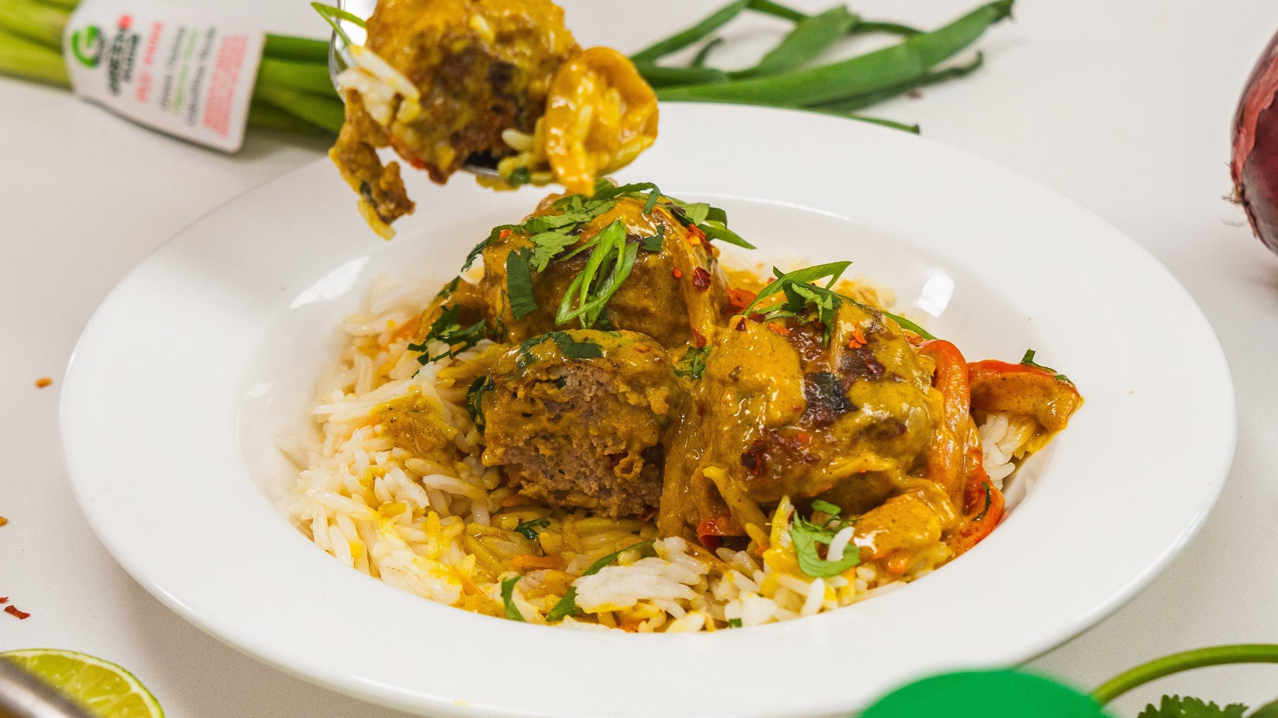 a white bowl with chicken meatballs and rice sitting on a counter. A fork with some food on it is on top of the bowl.