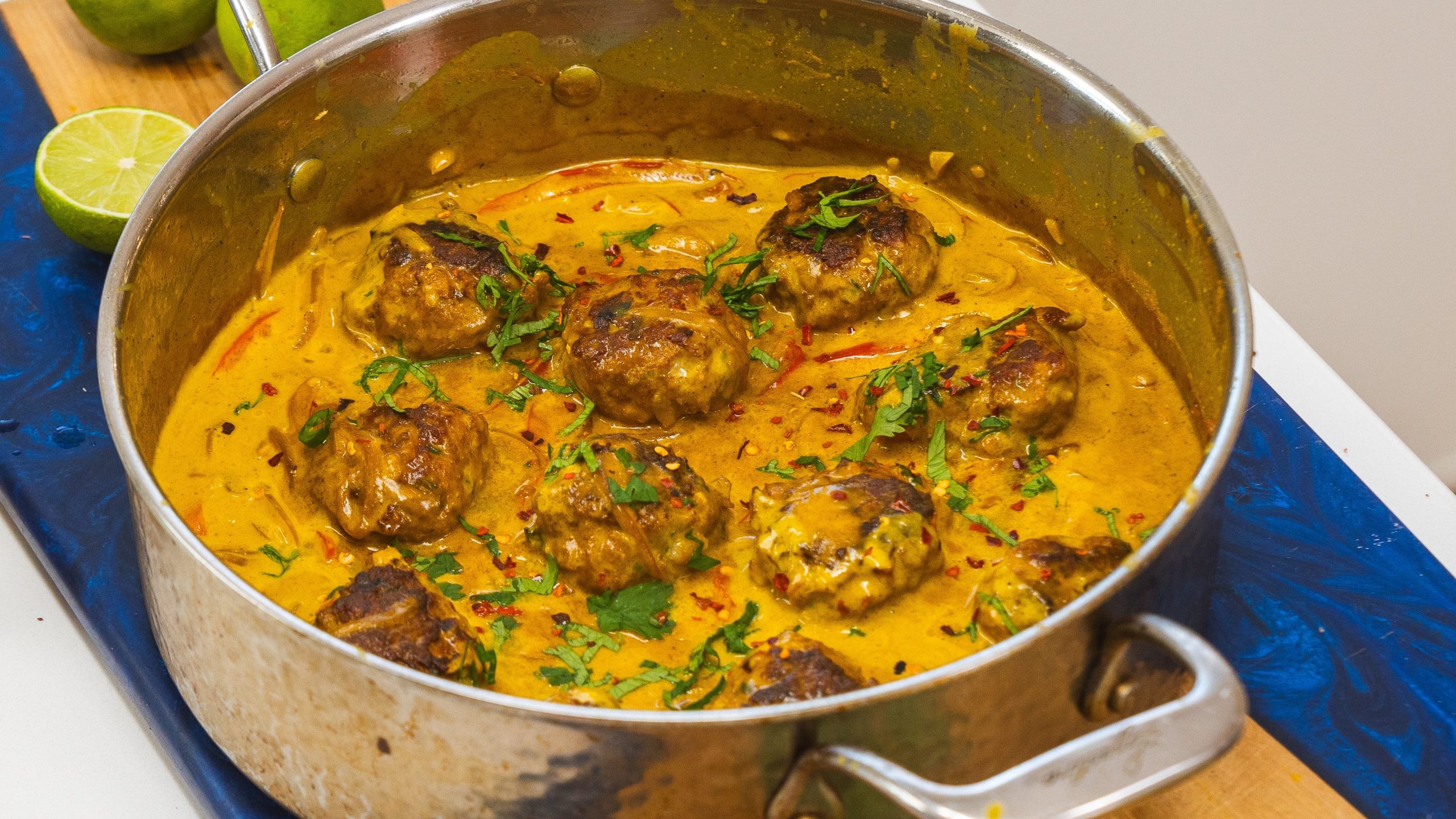 A stainless steel pot filled with Thai chicken meatballs in sauce, sitting on a counter top.