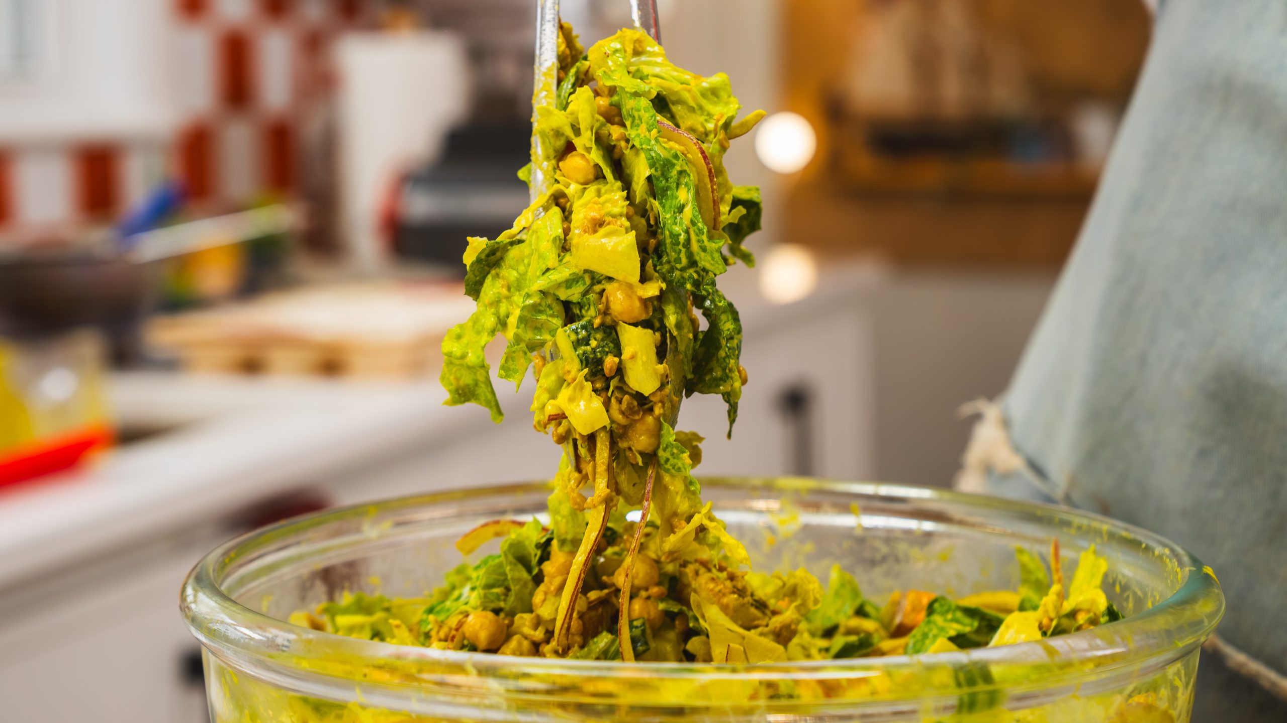 Tongs lifting a scoop of halloumi's salad with tahini salad dressing from a large clear bowl. This is a colourful and delicious Middle Eastern Salad.