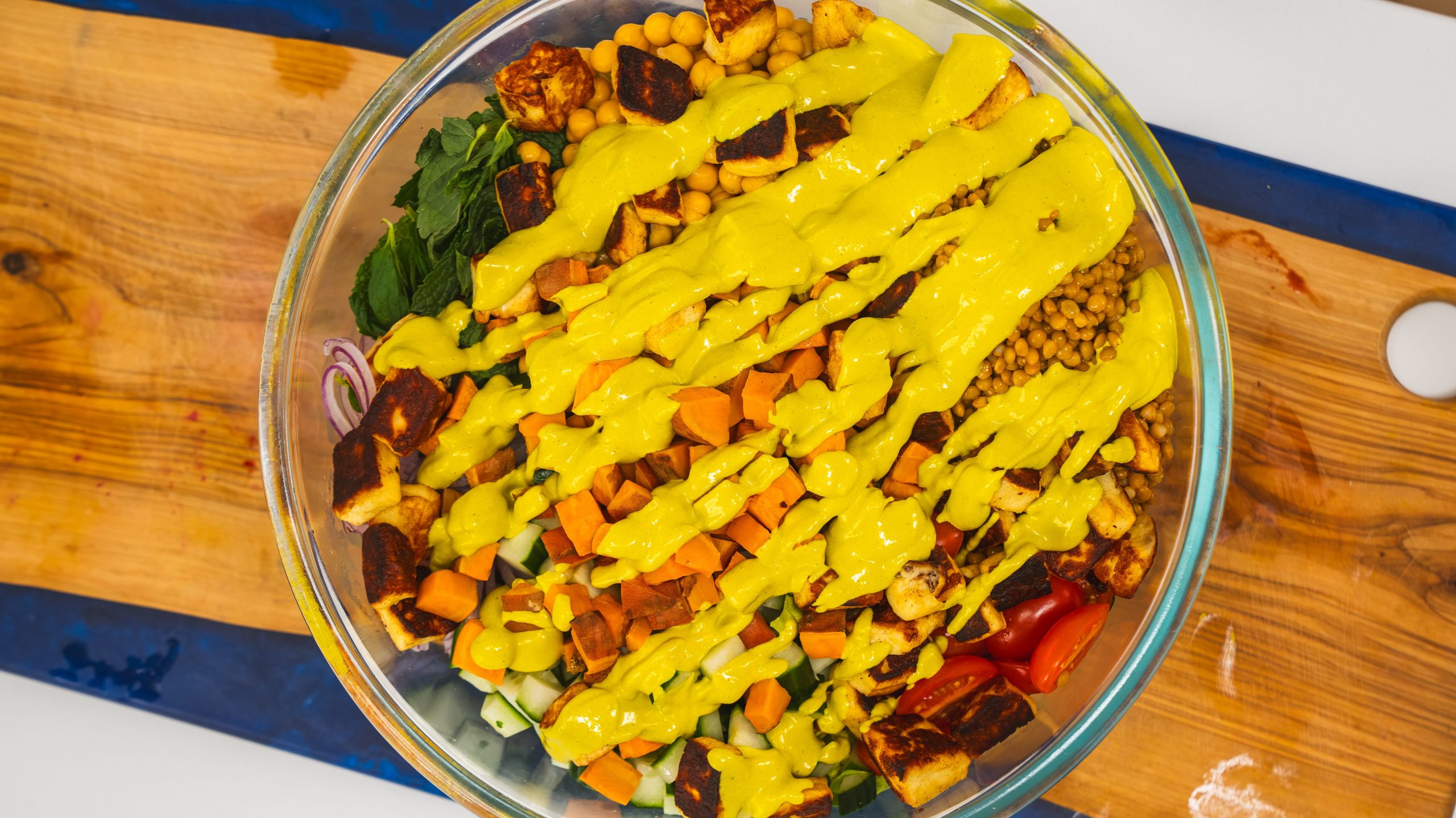 A Middle Eastern Salad in a large clear bowl with fresh vegetables and a tahini salad dressing.