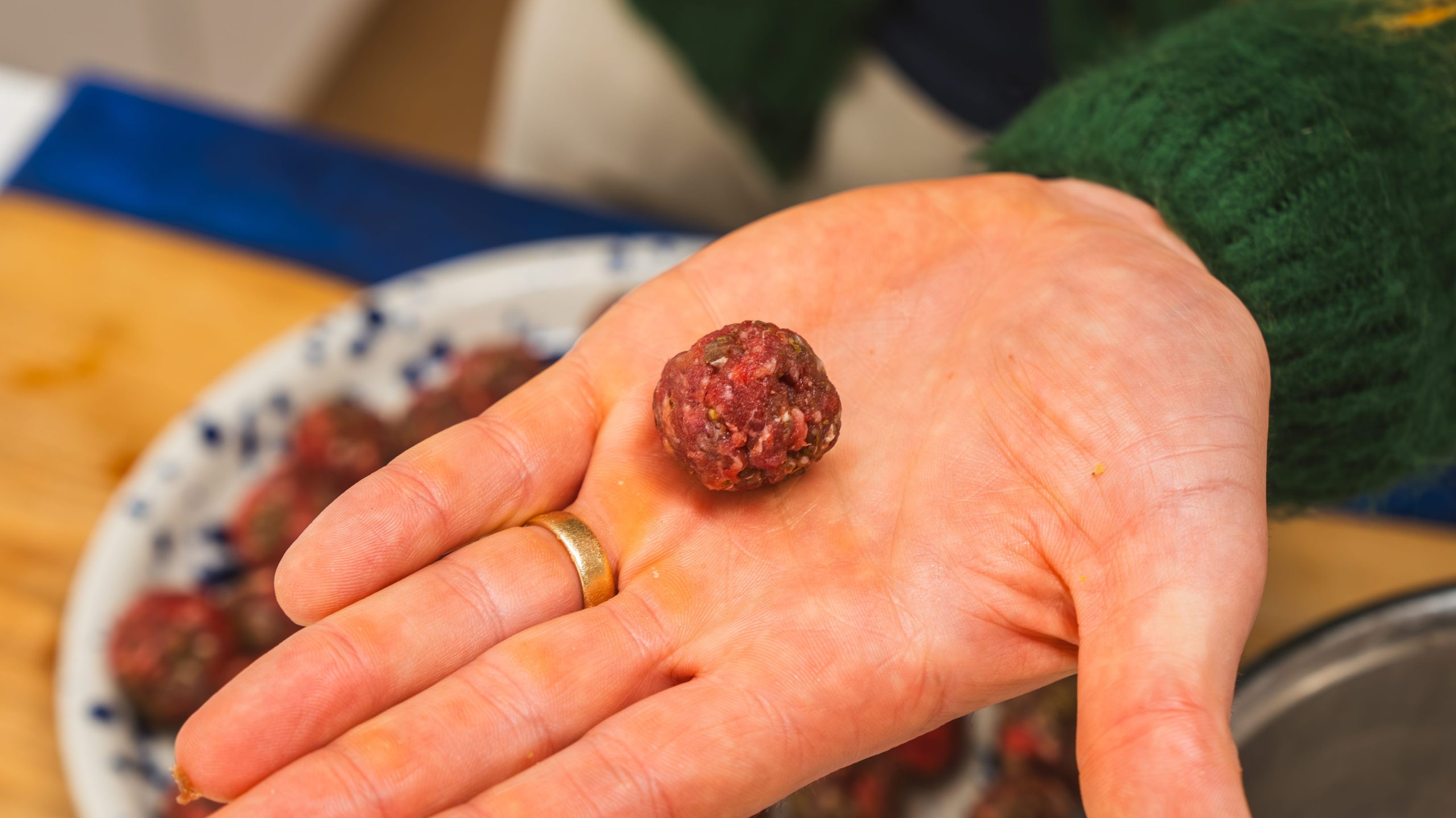 A hand holding a perfectly shaped meatball for Italian Wedding Soup.