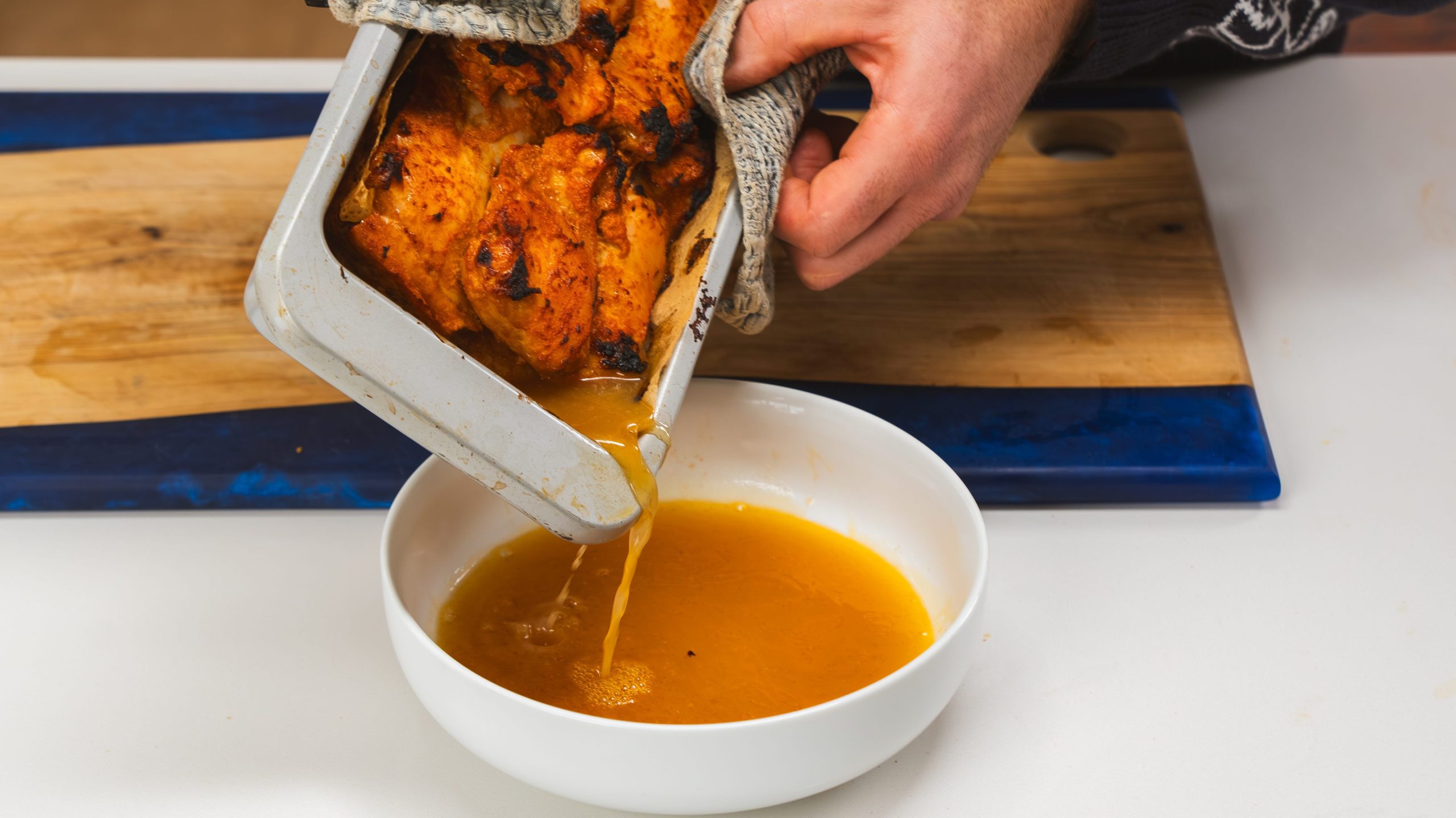 A loaf pan filled with chicken Sharma with the juices being poured off into a bowl.