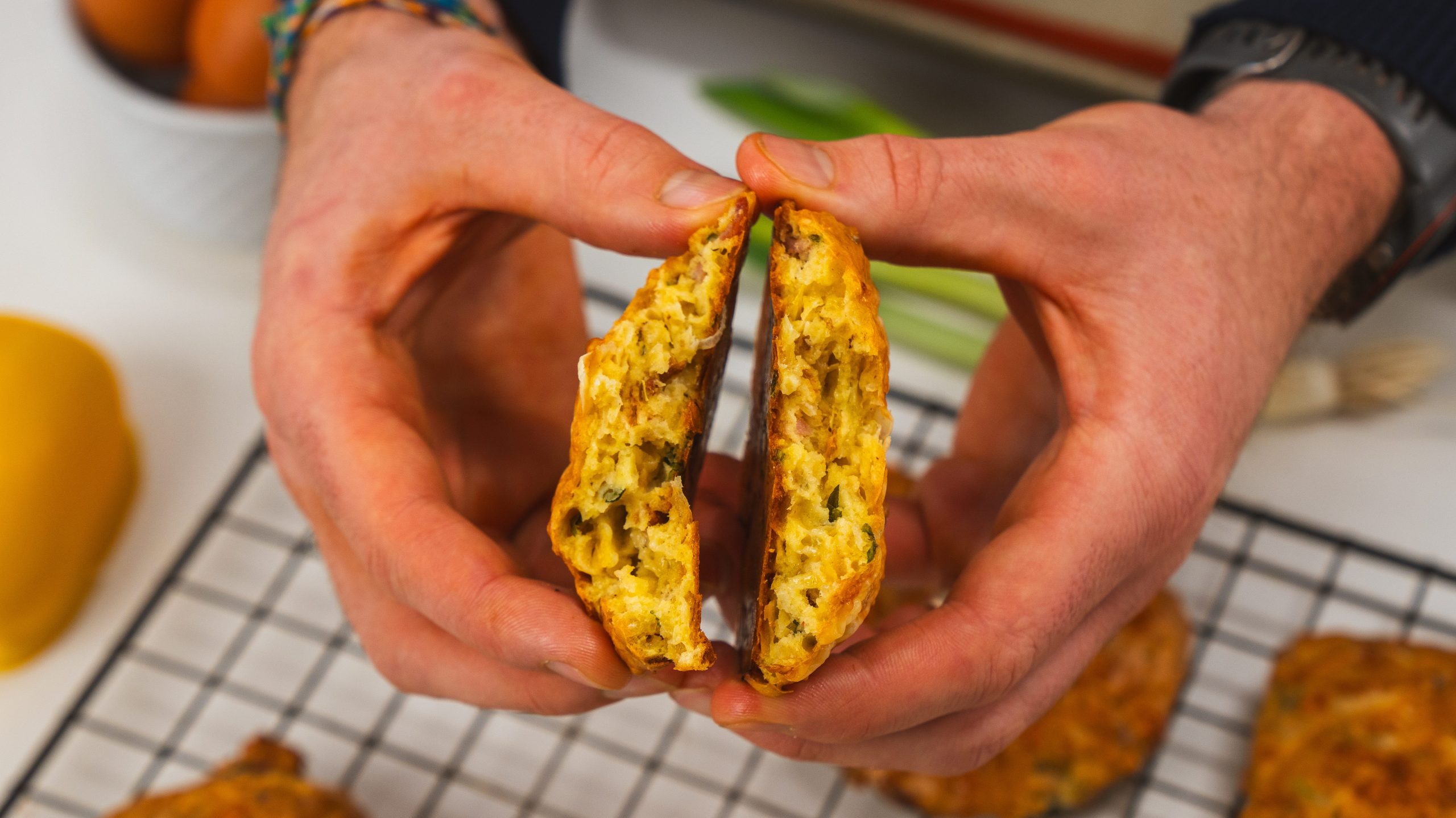A man holding two cheesy breakfast biscuits over a wire rack.