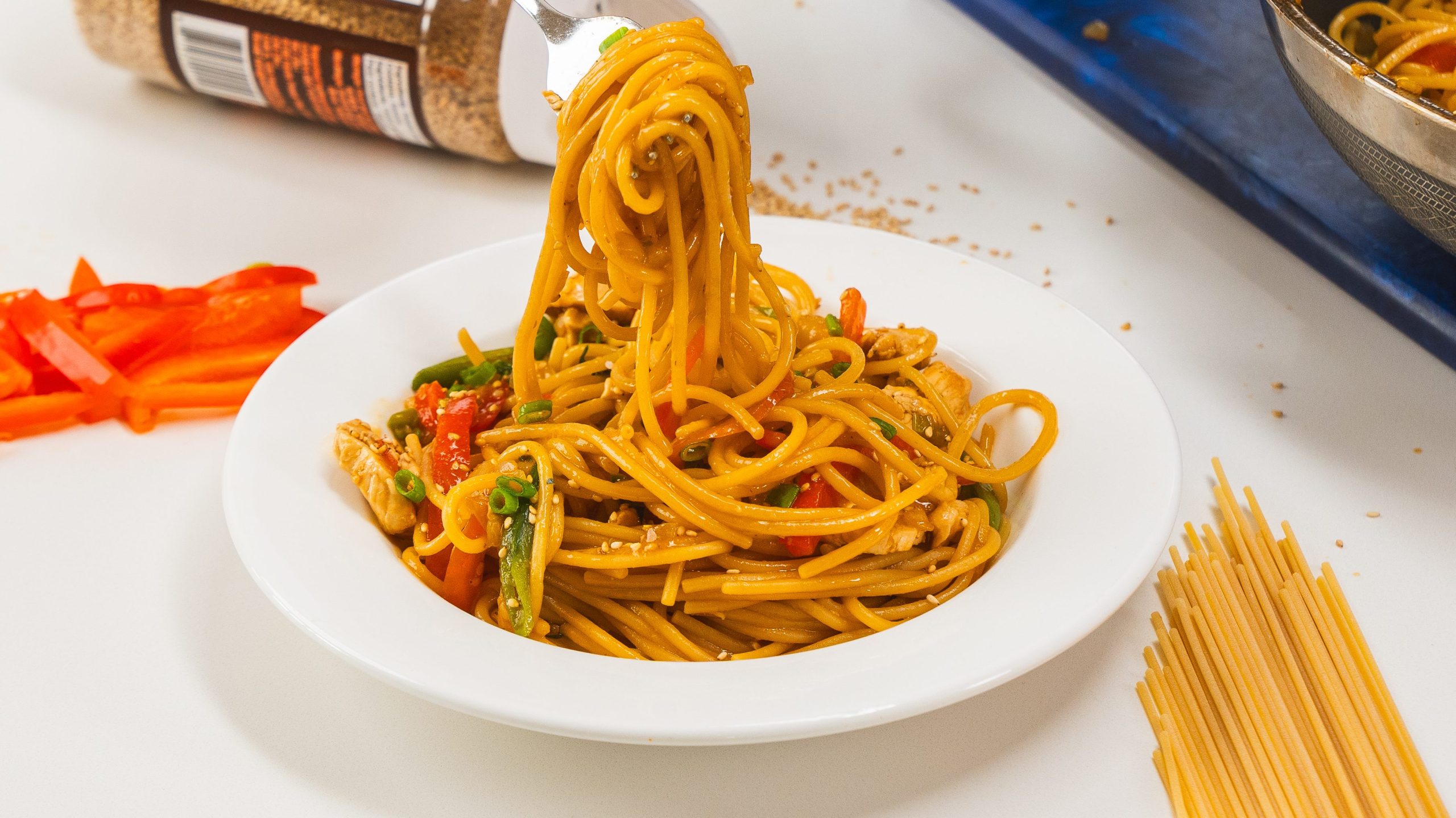 Noodles in a white bowl with a fork over top twirling some of the noodles.