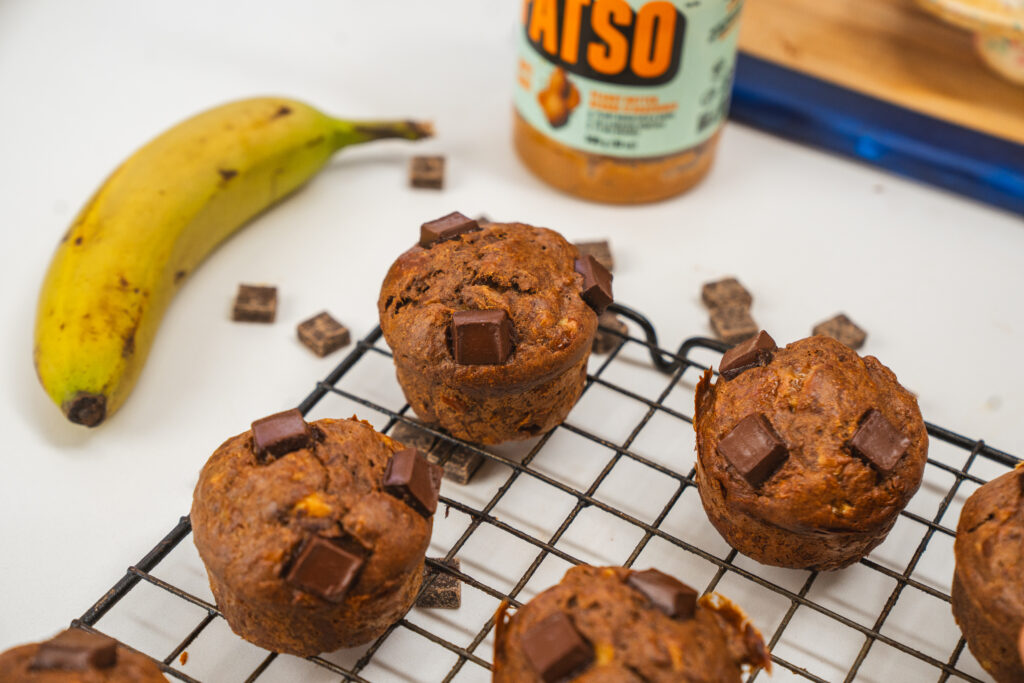 Peanut butter banana muffins with chocolate chunks on top, sitting in a wire rack