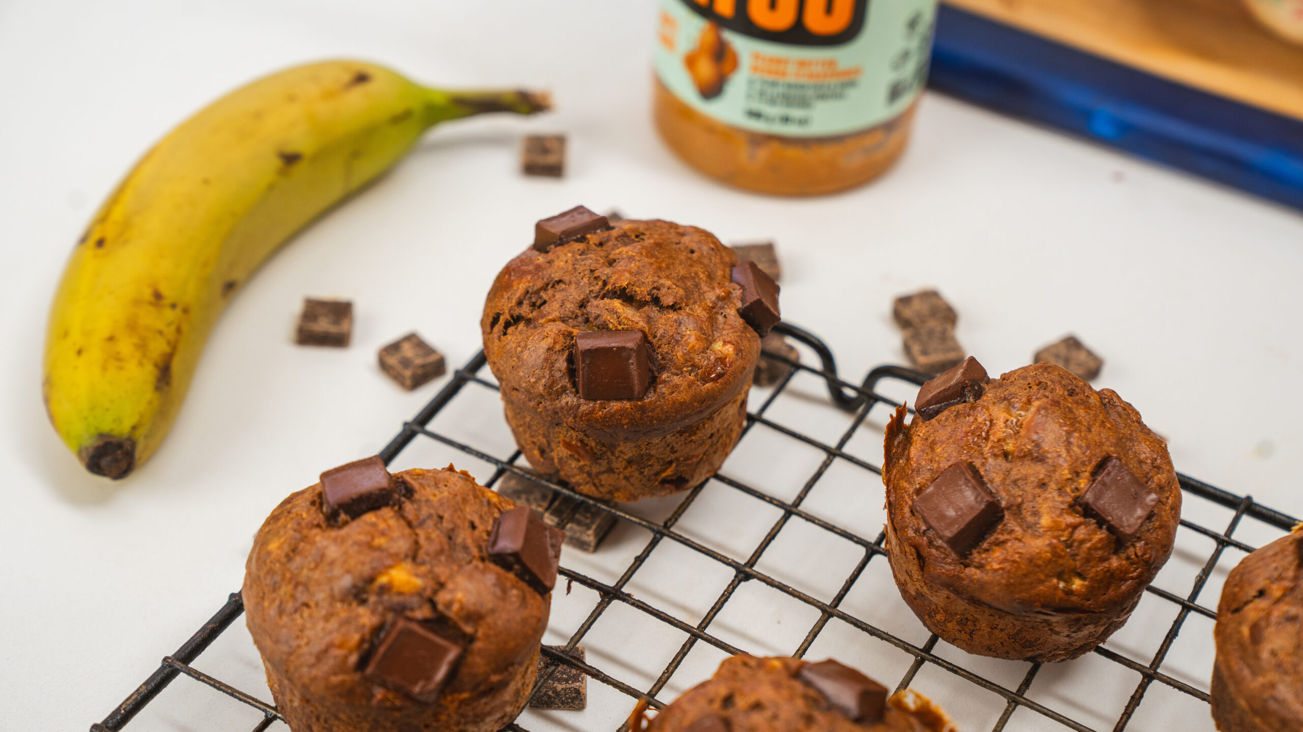 Peanut butter banana muffins with chocolate chunks on top, sitting in a wire rack